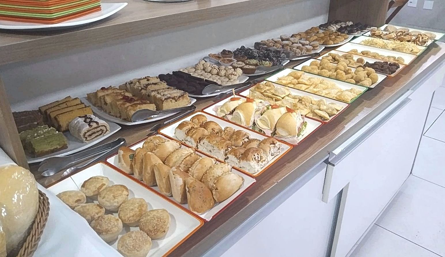 Balcão com bandejas de mini sanduíches, empadas, bolos e doces para coffee break corporativo